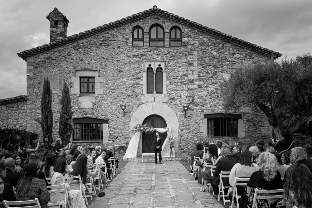 Ceremonia al aire libre con invitados sentados frente a una masía de piedra