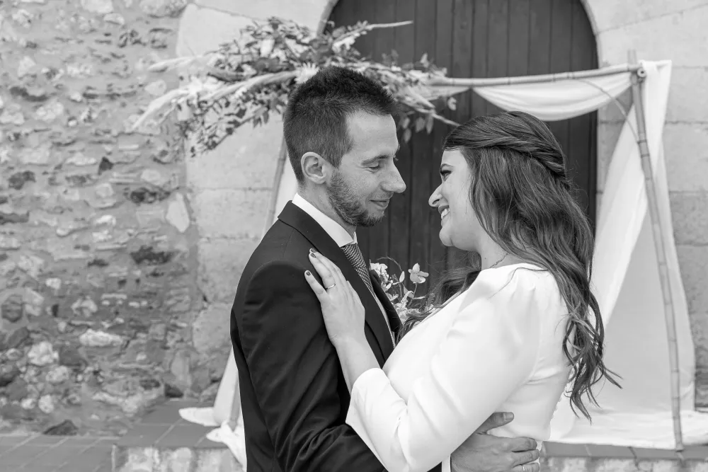 Novios abrazados bajo un arco de piedra con flores