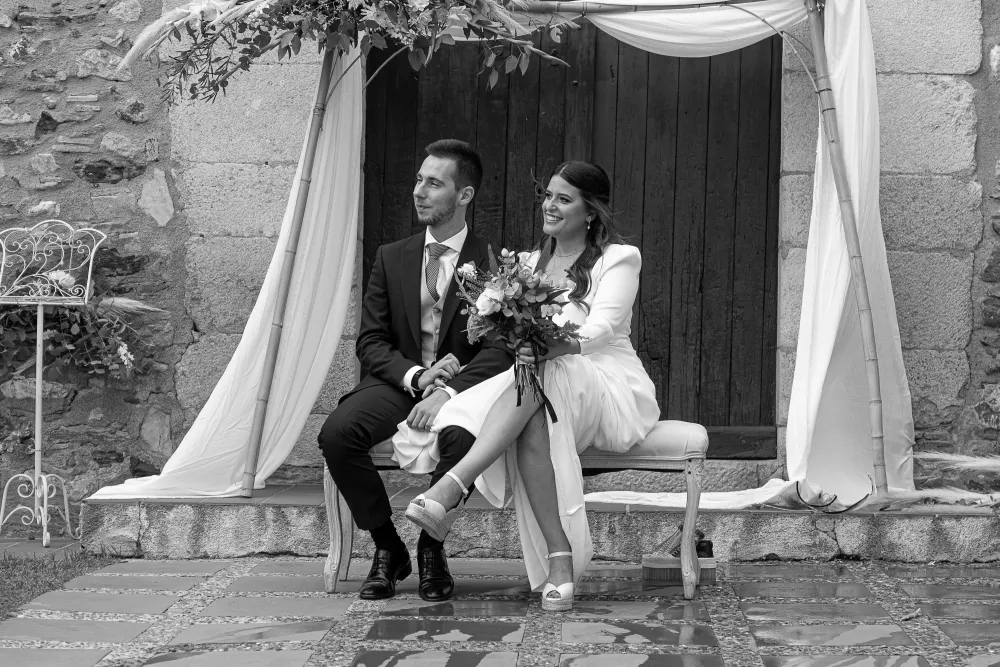 Novios sentados en un banco bajo un dosel de tela en el jardín