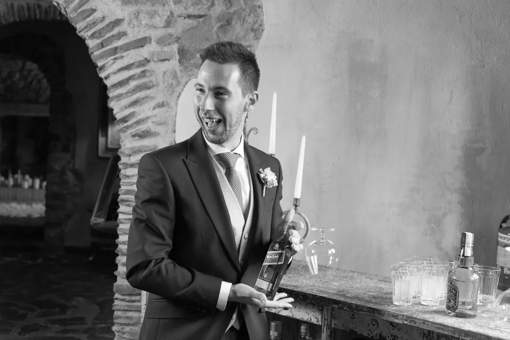 Novio riendo junto a unas velas en un salón con arcos de piedra