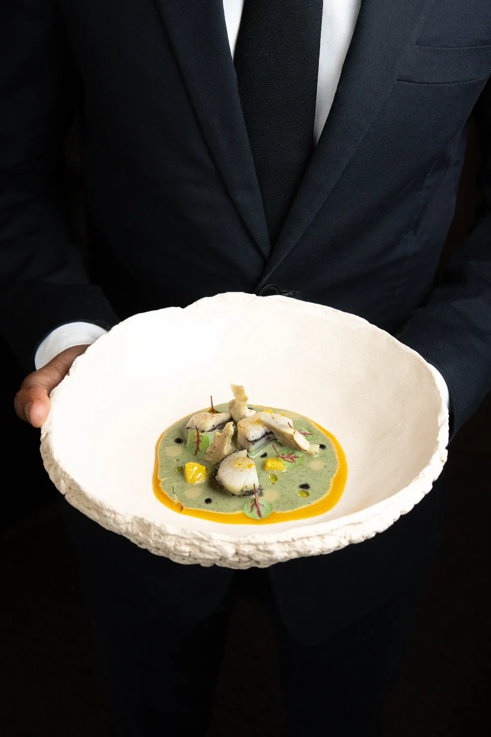 Plato de alta cocina con verduras y gotas de salsas de colores sobre un plato blanco de borde dorado