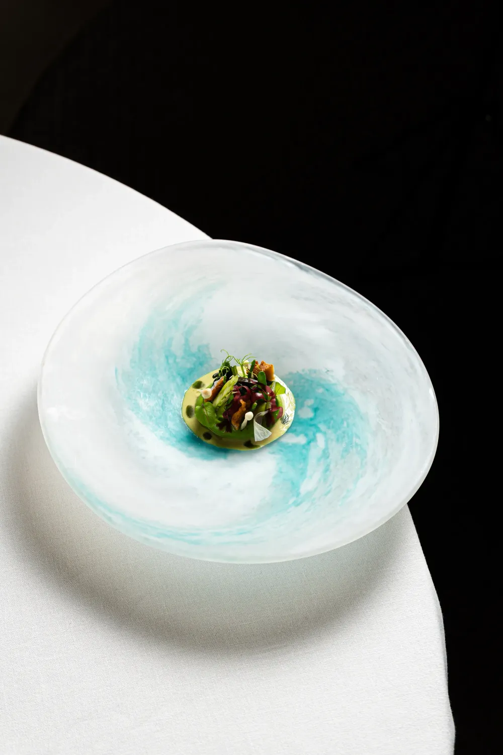 Plato de cocina creativa servido en un cuenco de cristal azul y blanco sobre un mantel blanco