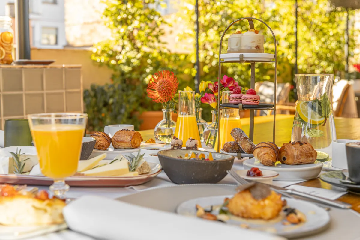 Mesa de desayuno en un restaurante con bollería, zumos y quesos con luz natural